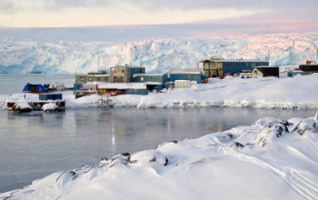 A cluster of buildings next to the ocean, surrounded by glaciers and snow.
